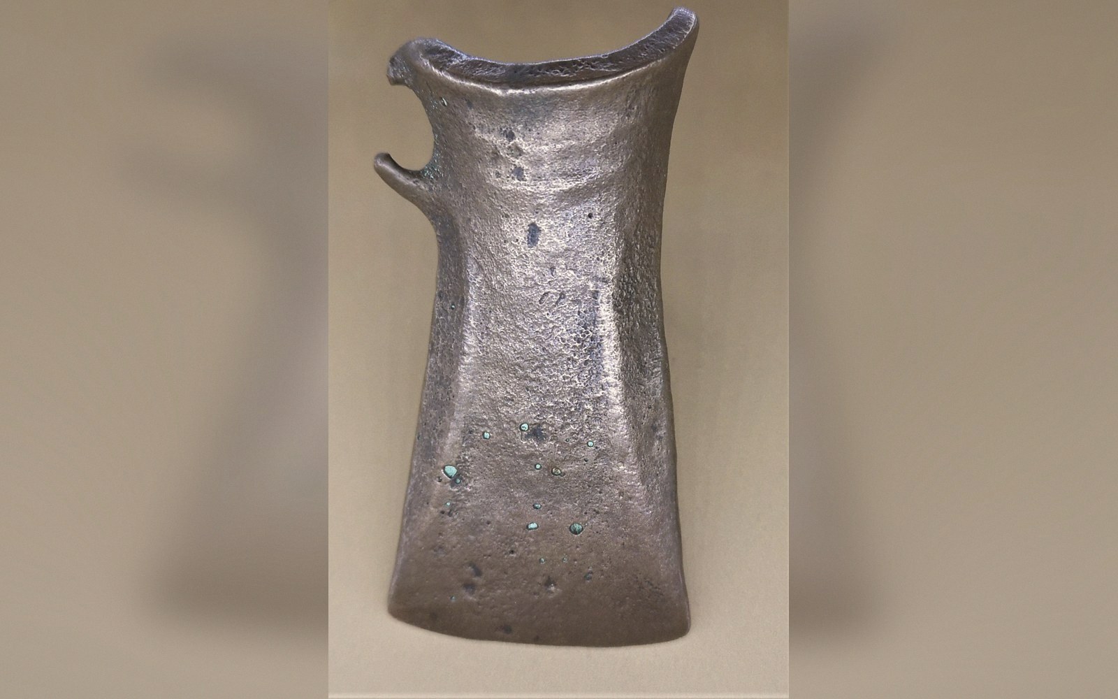 A corroded bronze socketed axe head with a flared, split-socket top