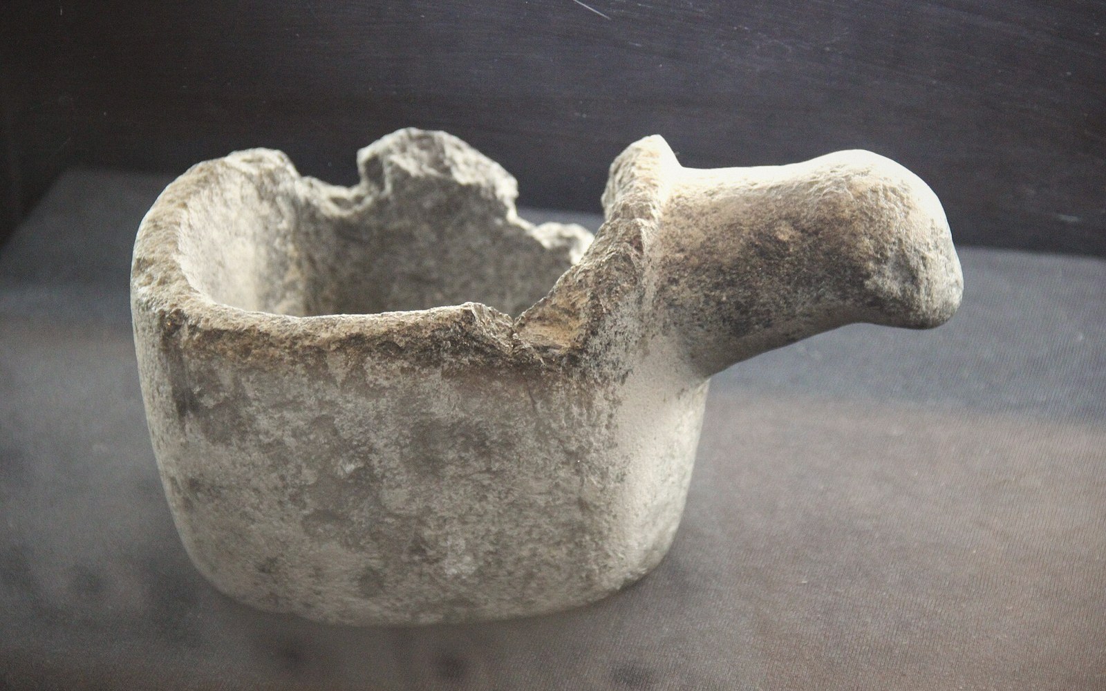 A weathered ceramic crucible with a chipped rim and pouring lip on display