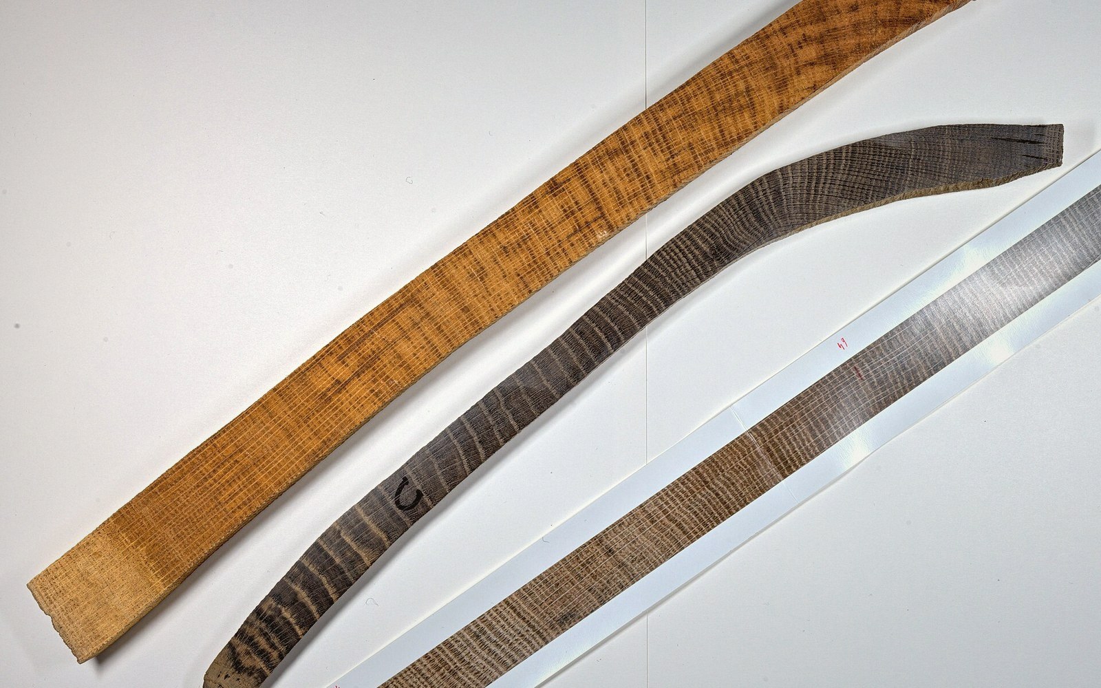 Three curved wooden strips showing tree ring grain patterns arranged diagonally on a white surface