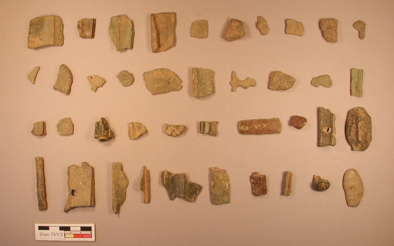 Rows of corroded metal fragments and shards arranged on a table beside a scale bar
