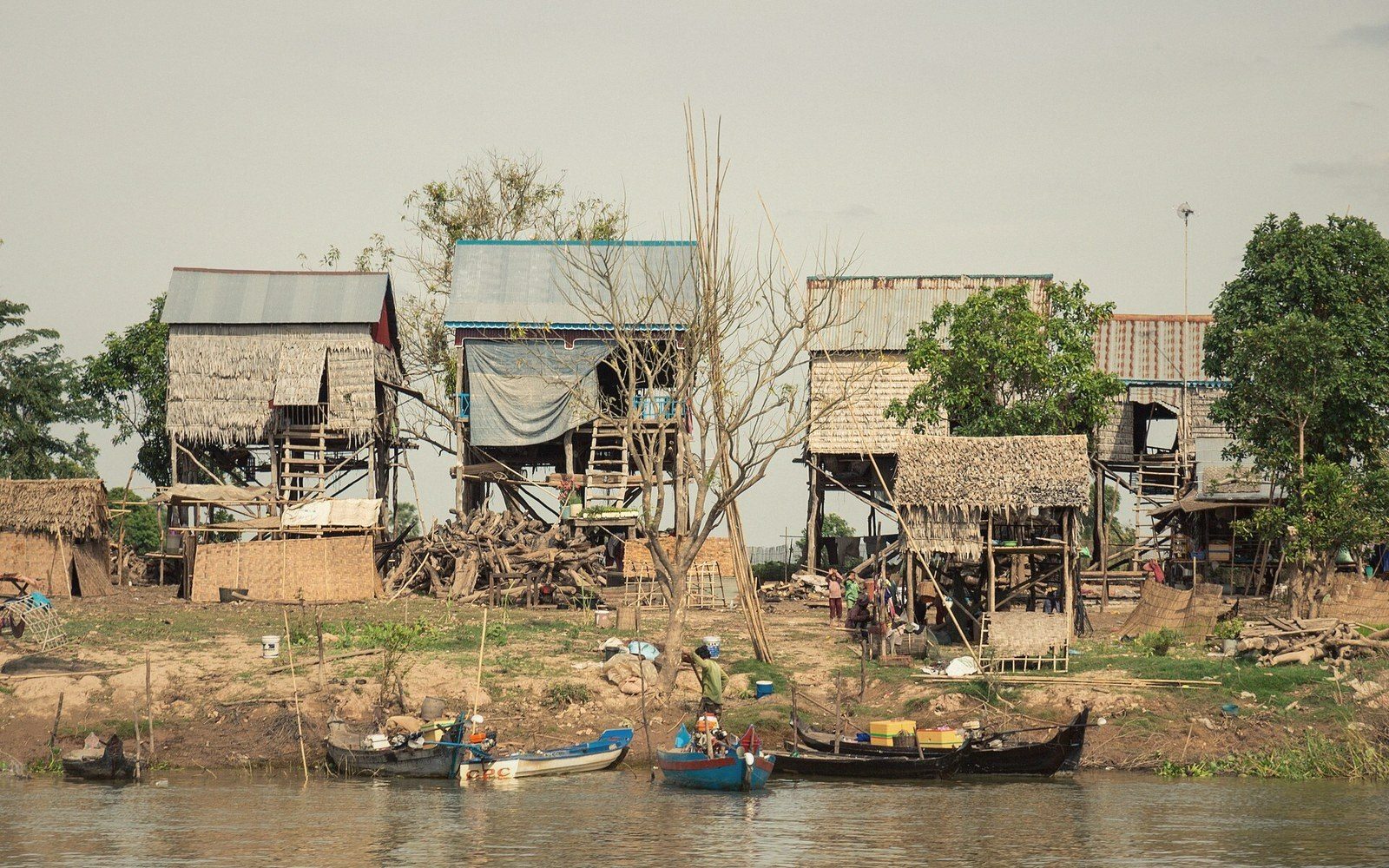 Stilt houses on a riverbank with small wooden boats moored along the shore