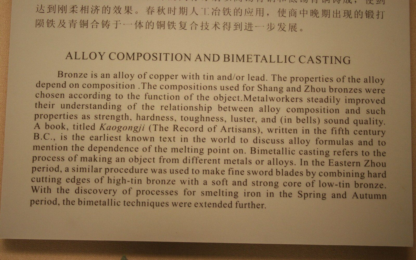 Museum placard explaining bronze alloy composition and bimetallic casting techniques in Chinese metalwork
